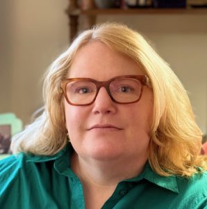 A photo of a woman with shoulder length hair wearing glasses and a green shirt