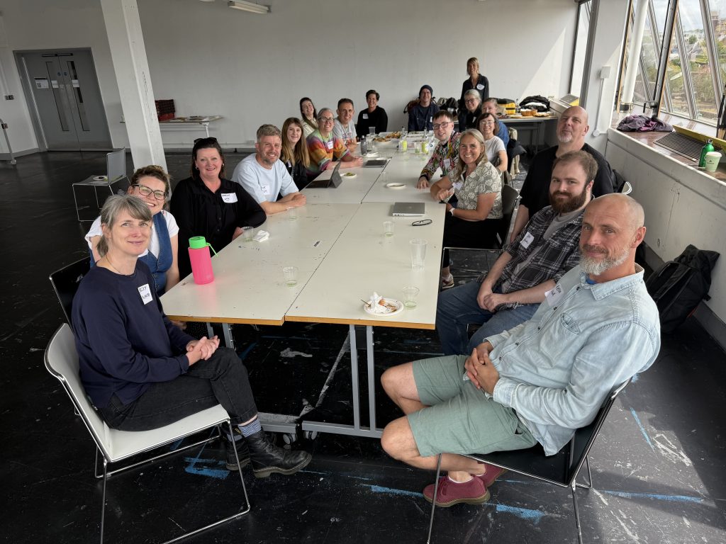 A photo of a group of people sitting around a table looking towards the camera.