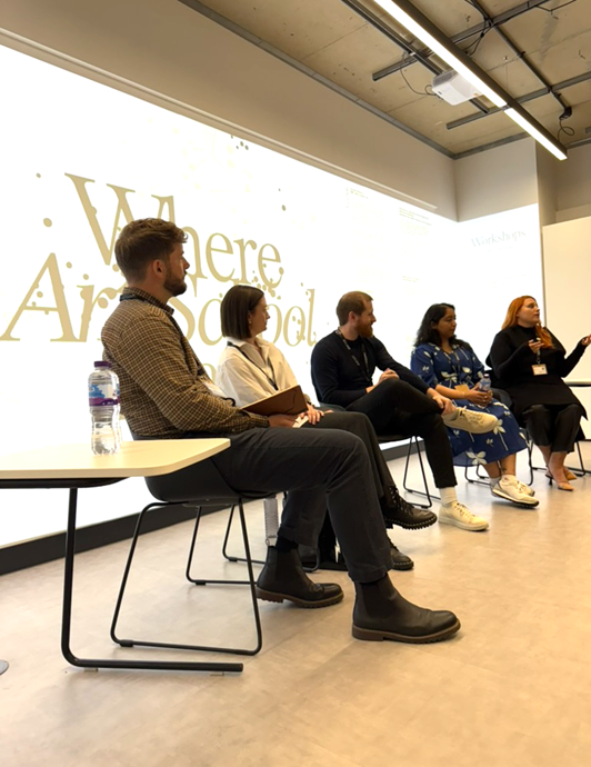 five people sat in a panel discussion in front of a lit background