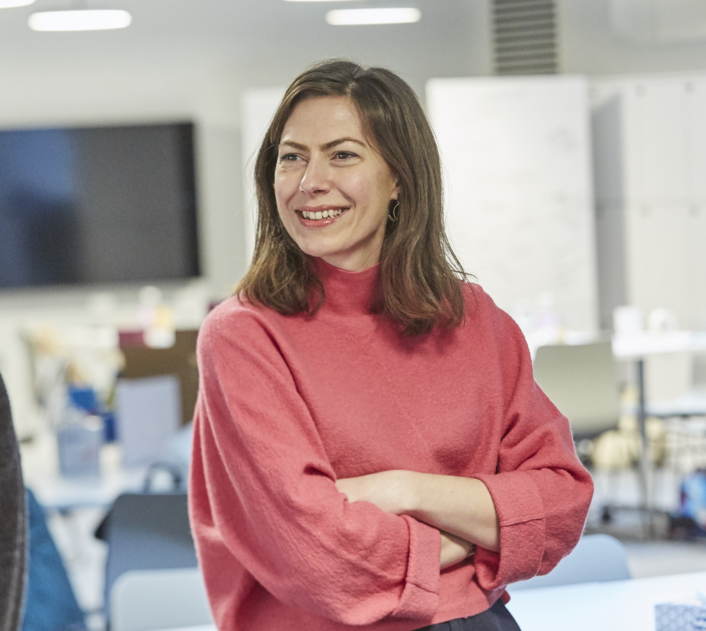 A photo of a woman with shoulder length brown hair wearing a pink jumper.